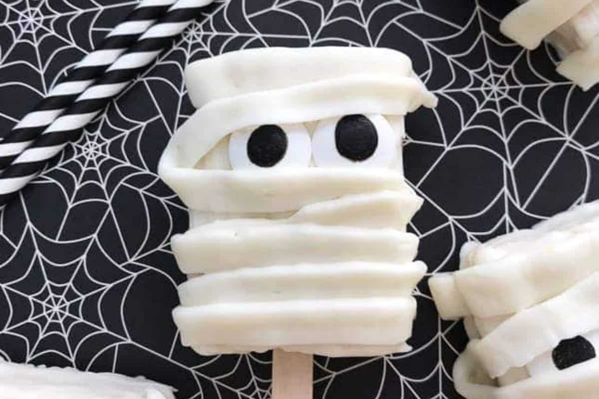 Rice Krispie treats covered in white icing strips to resemble mummies, with small candy eyes peeking through.