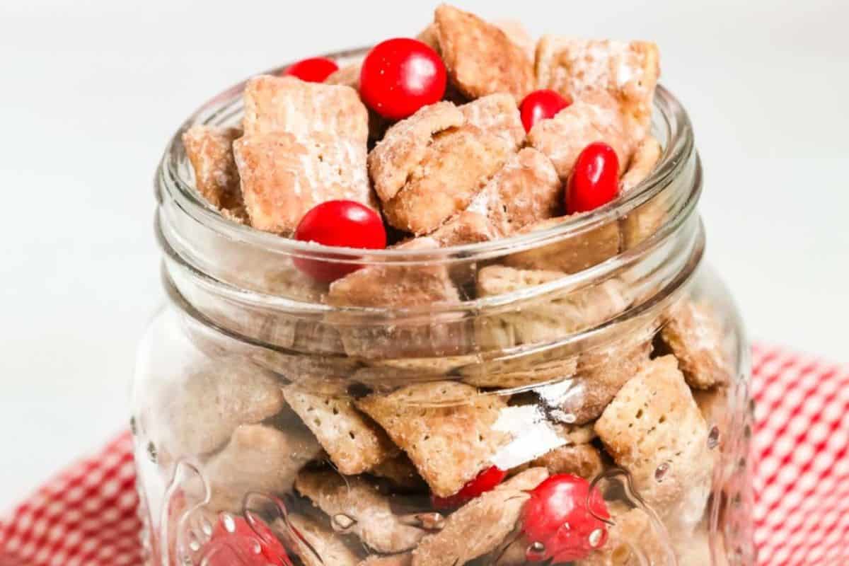 A glass jar filled with the red velvet chex muddy buddies recipe.