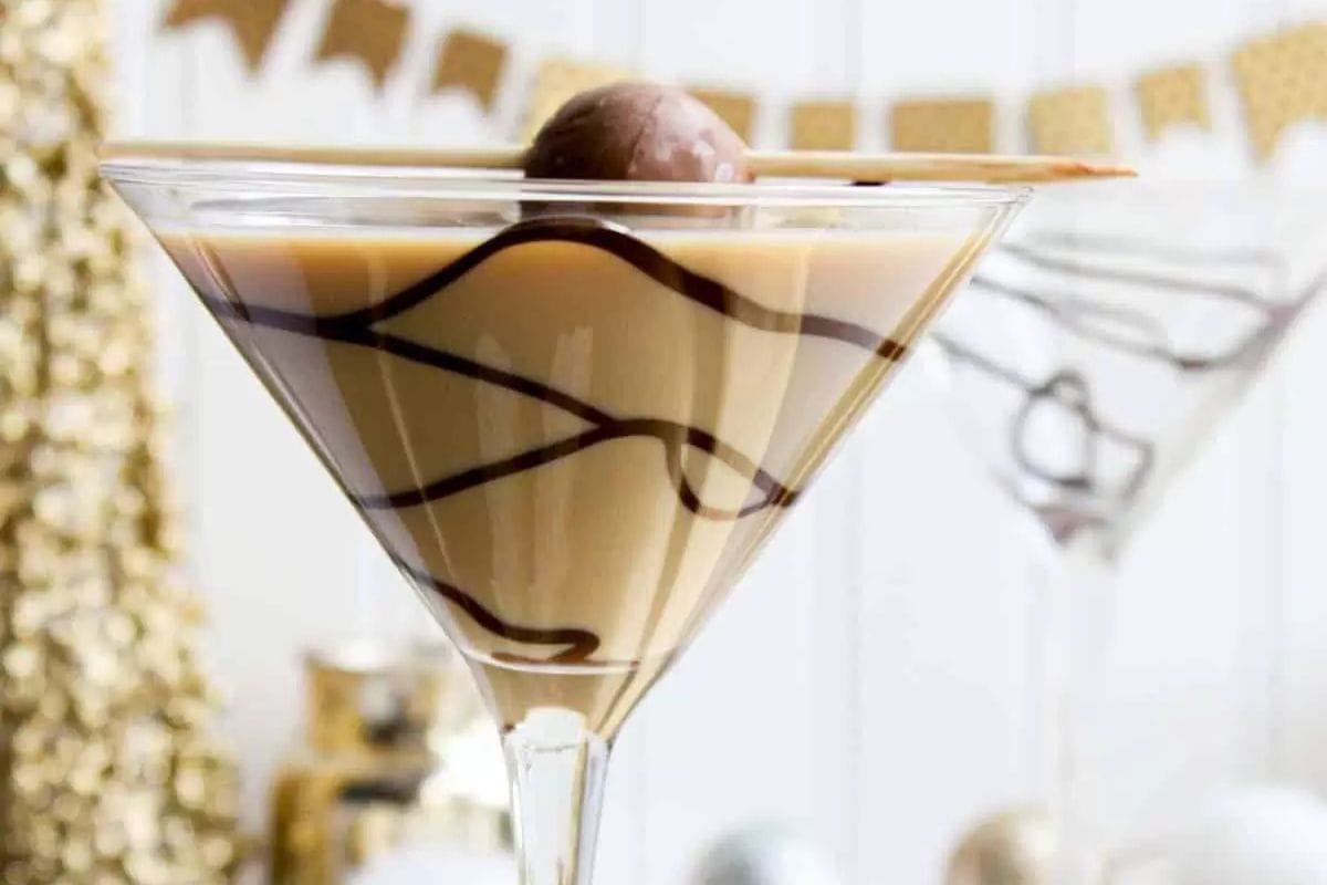 A martini glass filled with a creamy brown cocktail, drizzled with chocolate syrup, and garnished with a chocolate truffle and a stick—perfect for those who love indulgent fall drinks and cozy seasonal cocktails.