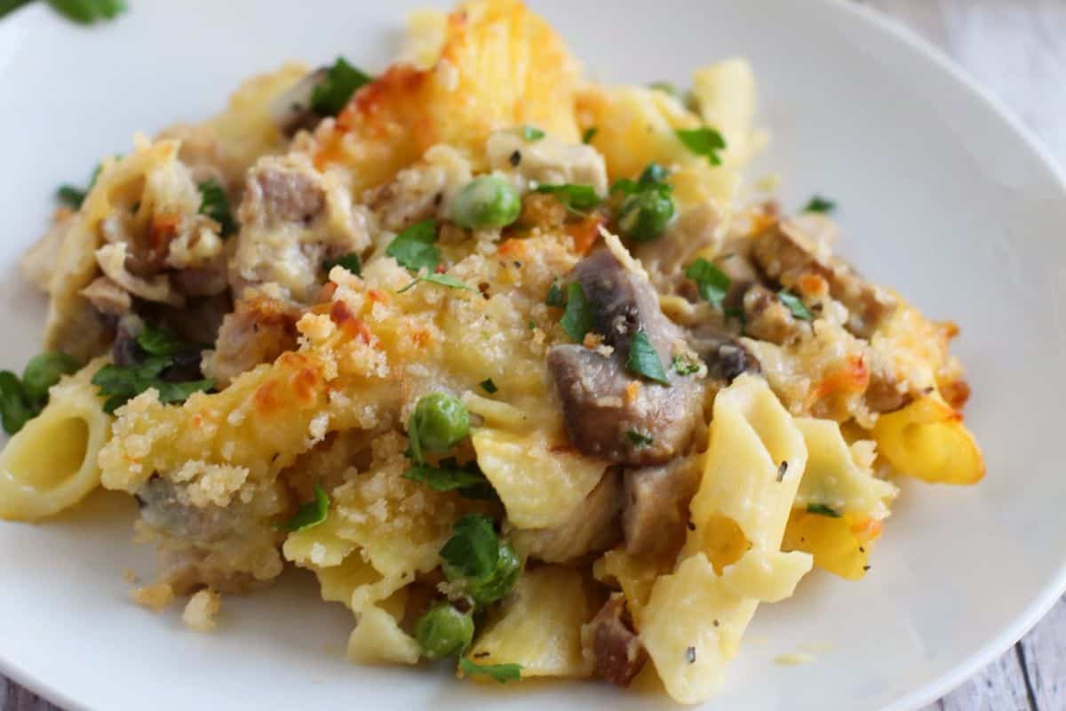 A plate of baked pasta casserole with mushrooms, peas, cheese, and breadcrumbs, garnished with chopped herbs—a perfect choice for comforting fall meals.