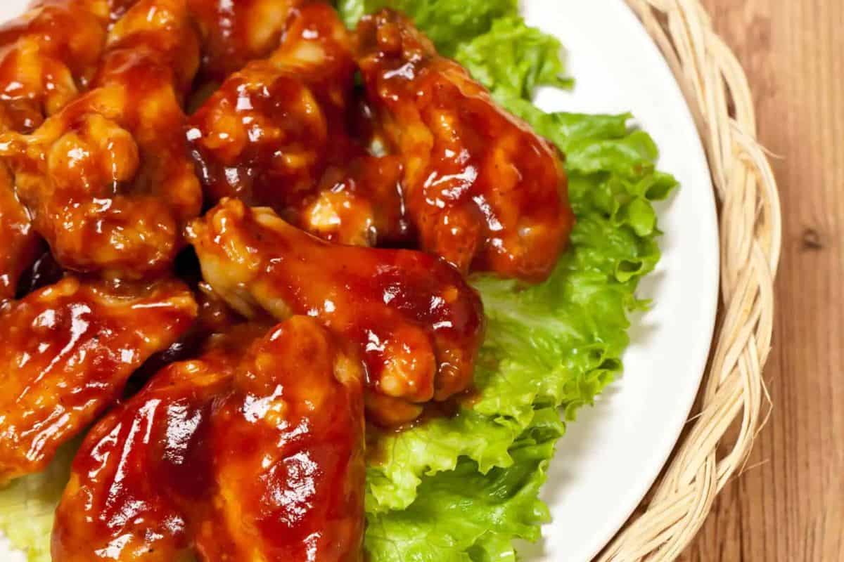 A plate of glazed barbecue chicken wings on a bed of green lettuce.