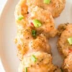 A close-up view of the appetizer coated in a creamy sauce, garnished with chopped green onions, and served on a white plate.