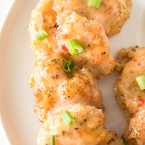 A close-up view of the appetizer coated in a creamy sauce, garnished with chopped green onions, and served on a white plate.