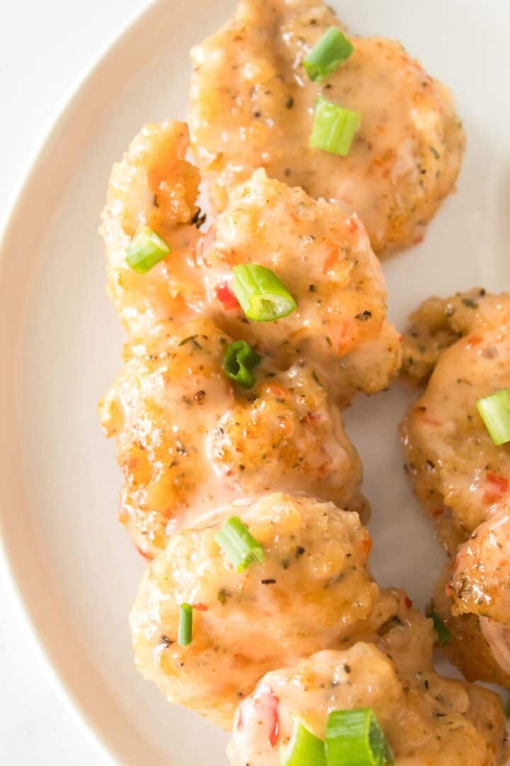 A close-up view of the appetizer coated in a creamy sauce, garnished with chopped green onions, and served on a white plate.