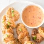 A plate of breaded, sauced nuggets inspired by Bang Bang Shrimp, garnished with chopped green onions and served next to a bowl of creamy orange dipping sauce.
