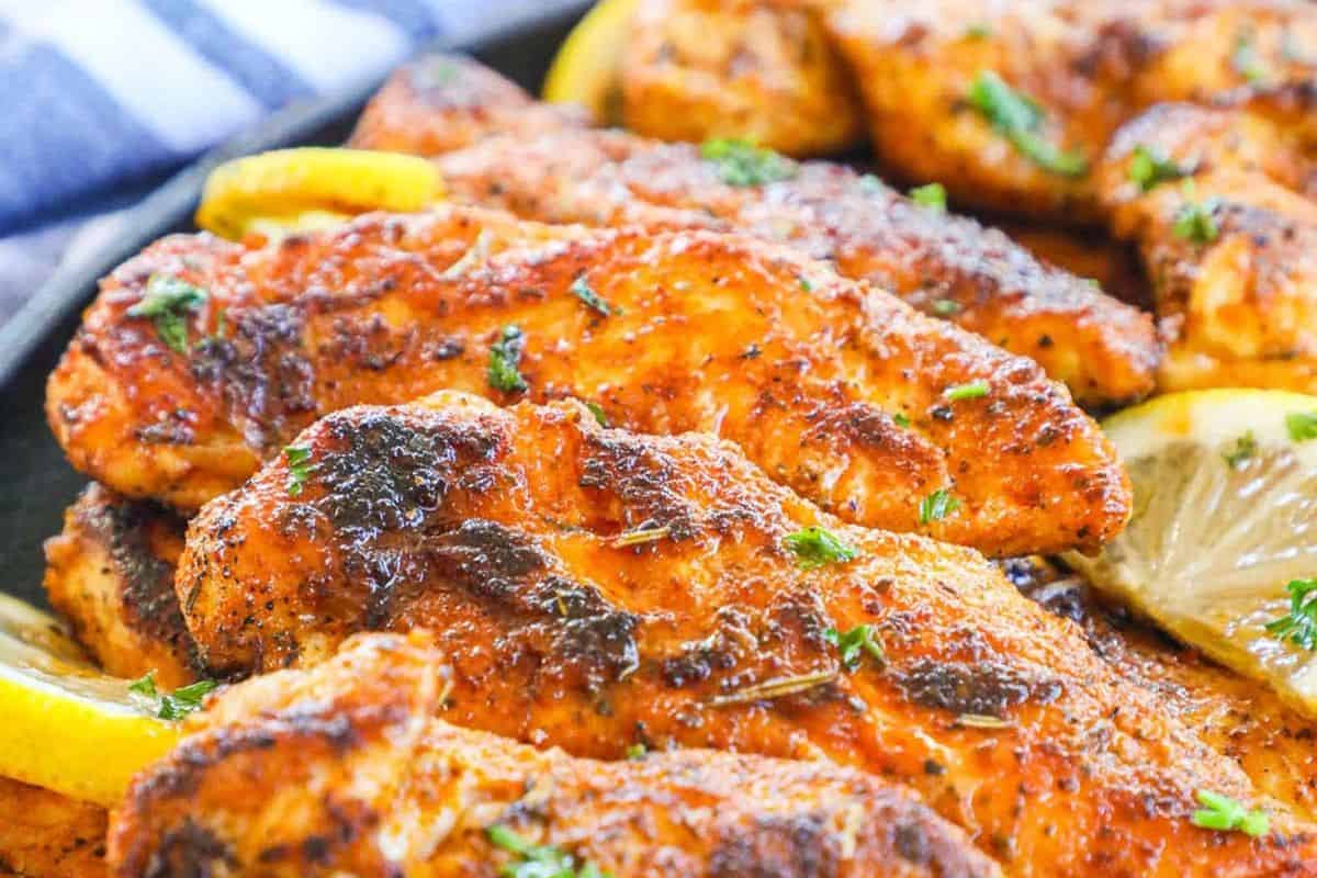 Close-up of seasoned, grilled chicken breasts—an easy favorite for cast iron recipes—garnished with chopped herbs and lemon slices.