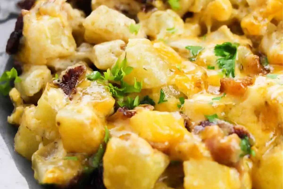 Close-up of cheesy potato casserole—perfect for breakfast recipes or dinner recipes—topped with chopped parsley and bits of bacon.