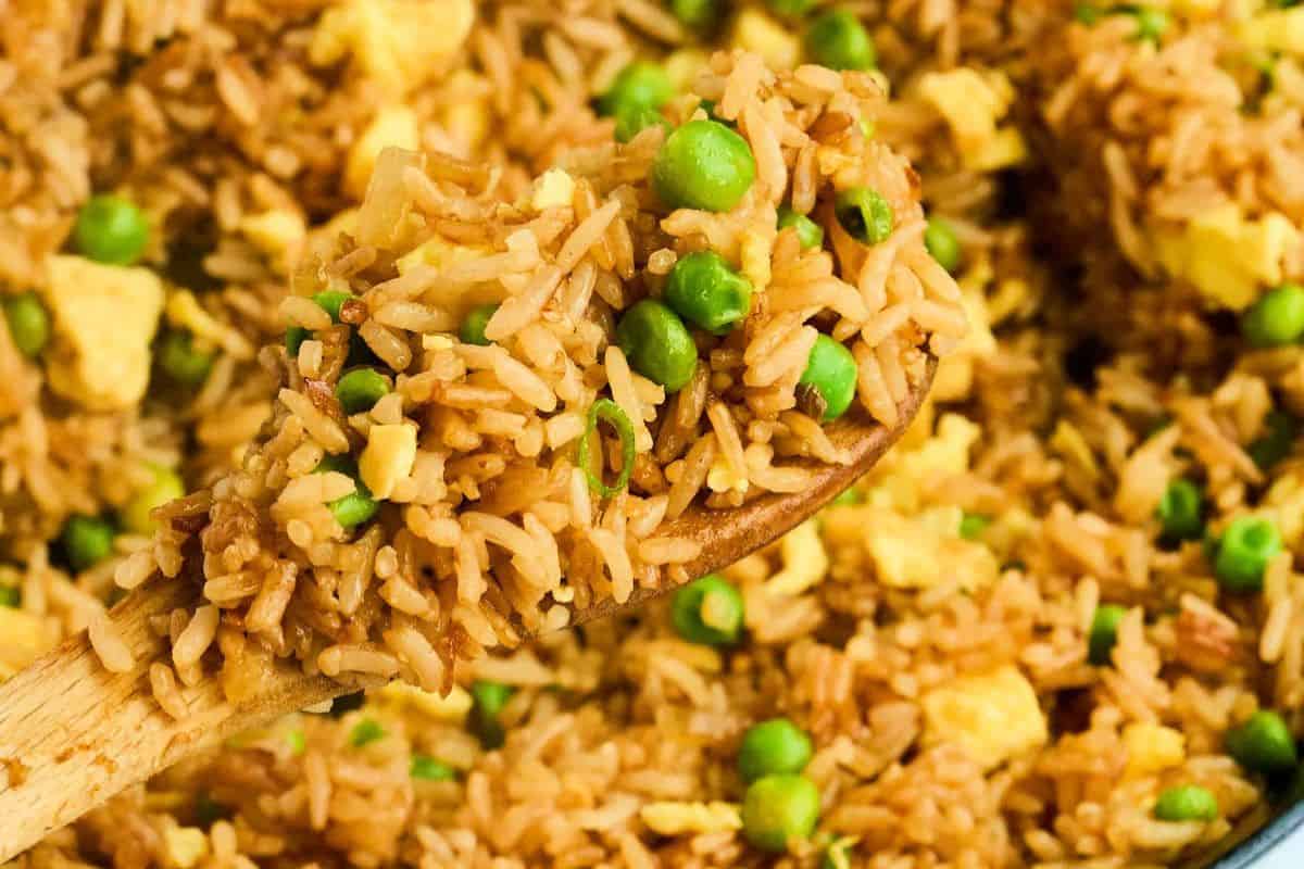 A wooden spoon holds a serving of fried rice mixed with green peas and scrambled eggs, perfect for those seeking quick and flavorful dinner recipes.