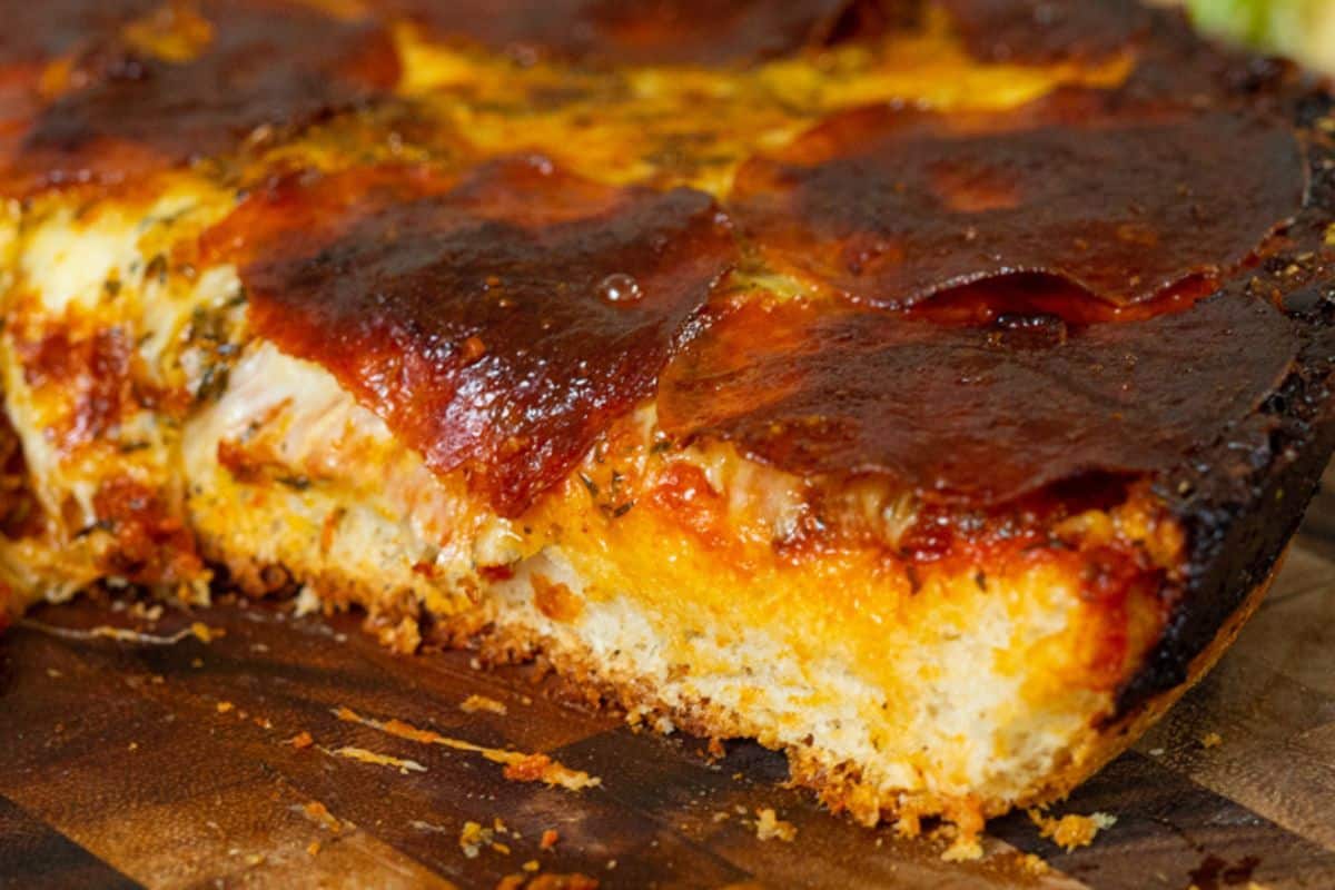 Close-up of a thick slice of Detroit-style pizza with crispy pepperoni, melted cheese, and a golden-brown crust on a wooden surface—perfect inspiration for cast iron recipes.