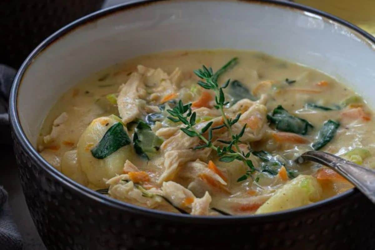 A close-up of some creamy turkey and gnocchi soup, served in a black and white bowl.