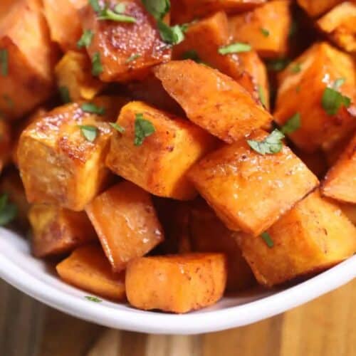 Close-up of roasted sweet potato cubes in a white bowl, garnished with chopped herbs, perfect for Sweet Potato Recipes to elevate your holiday table.
