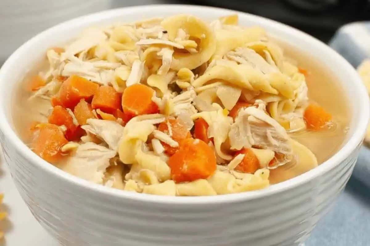 Close-up of a bowl of crock pot turkey soup, with carrots and noodles.