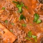 Close-up of Crockpot Short Ribs braised in beer, with tender chunks of meat, bone, chopped parsley, and a rich brown broth simmering in the pot.
