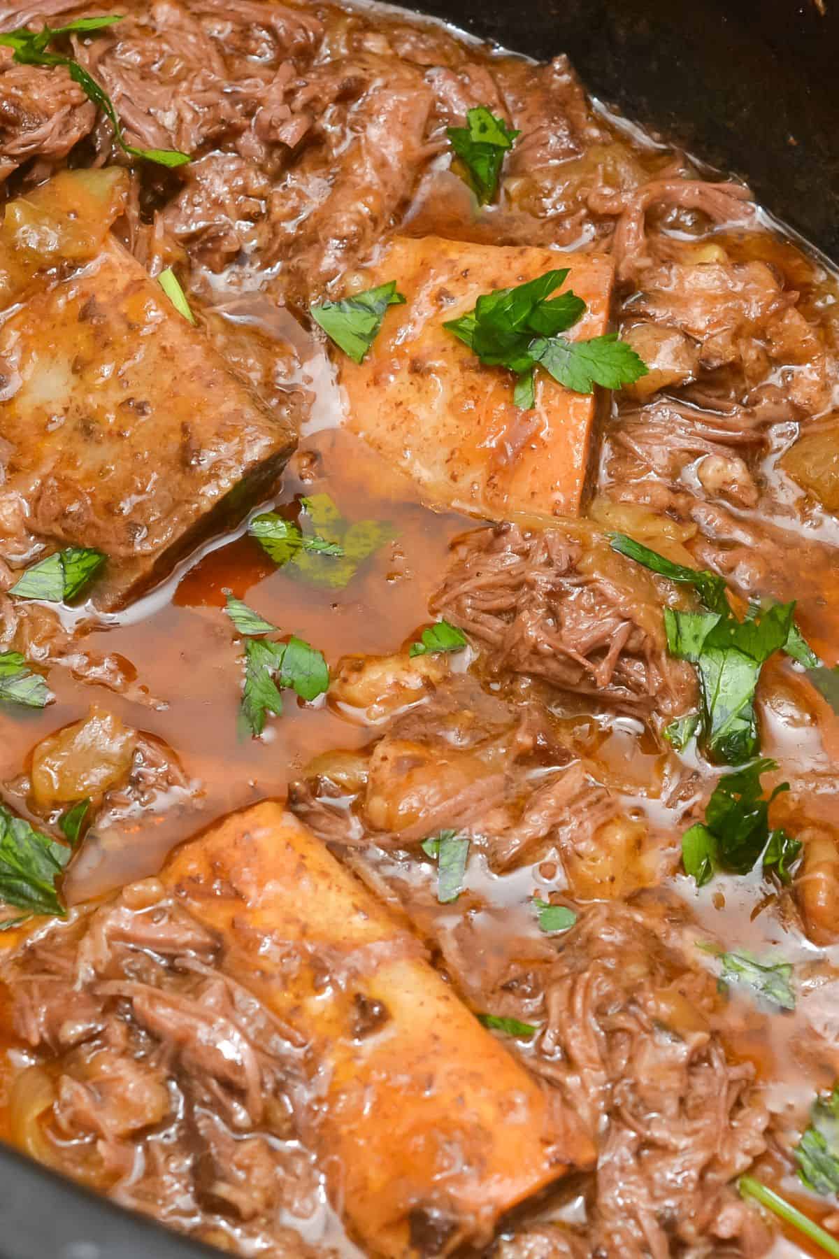 Close-up of Crockpot Short Ribs braised in beer, with tender chunks of meat, potatoes, and carrots in a rich brown sauce, garnished with chopped parsley.