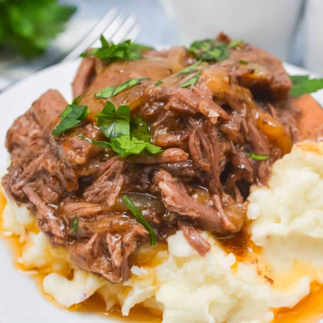 Shredded pot roast with brown gravy, reminiscent of Crockpot Short Ribs Braised in Beer, served over mashed potatoes and garnished with chopped parsley.