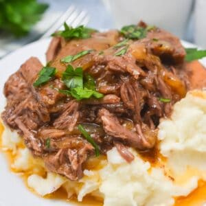 Shredded pot roast with brown gravy, reminiscent of Crockpot Short Ribs Braised in Beer, served over mashed potatoes and garnished with chopped parsley.