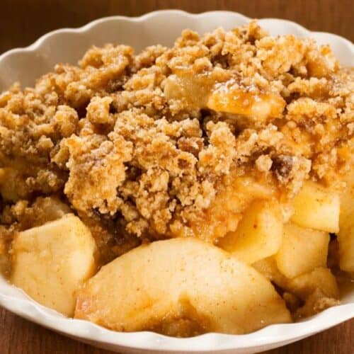 A white dish filled with Easy Apple Crumble, featuring sliced apples and a crumbly, golden brown topping.