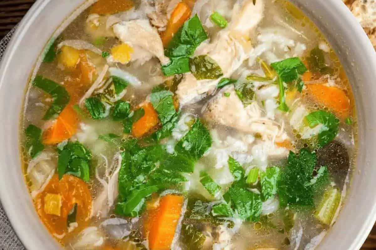 Close-up of a bowl of turkey rice soup, with carrots, spinach, and spinach.