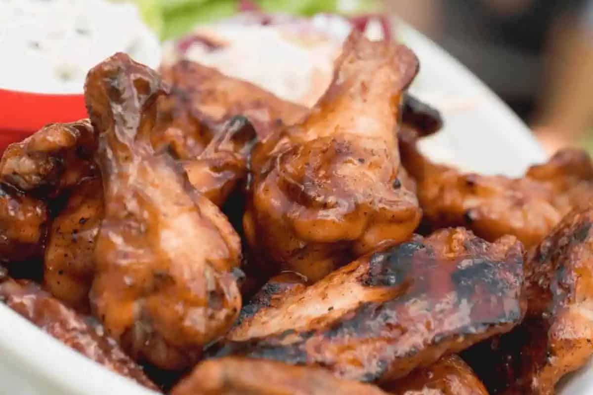 A plate of glazed, grilled chicken wings with a dip in the background.