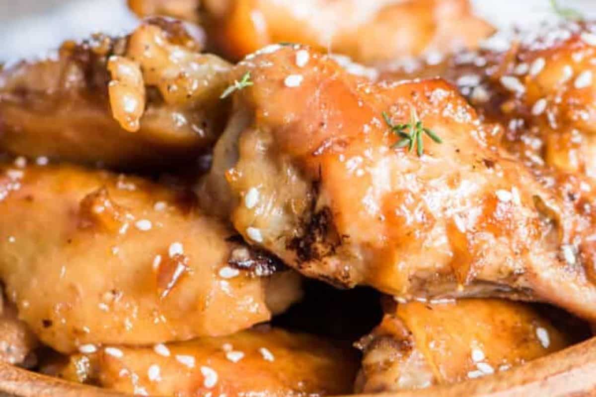 Close-up of glazed chicken wings sprinkled with sesame seeds and garnished with small herbs.