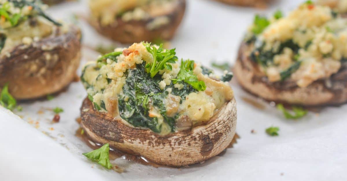 Stuffed Mushrooms filled with spinach and creamy Boursin cheese, mixed with fresh herbs, topped with golden breadcrumbs and garnished with parsley, all arranged on a parchment-lined baking sheet.