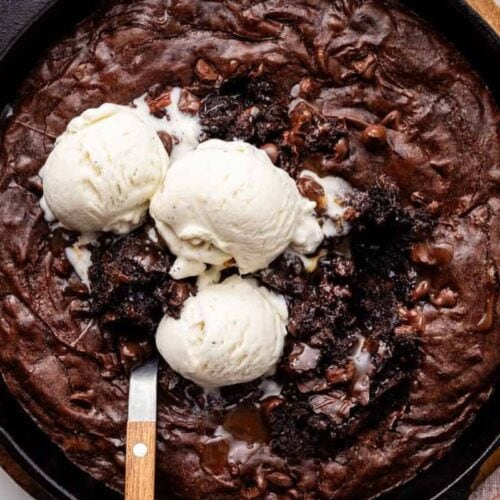 A decadent skillet brownie from our favorite cast iron recipes, topped with three scoops of vanilla ice cream and a spoon ready to dig in.