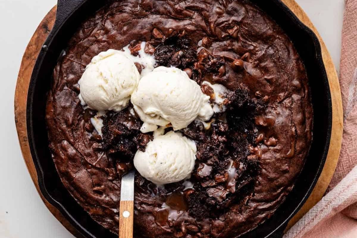 A decadent skillet brownie from our favorite cast iron recipes, topped with three scoops of vanilla ice cream and a spoon ready to dig in.