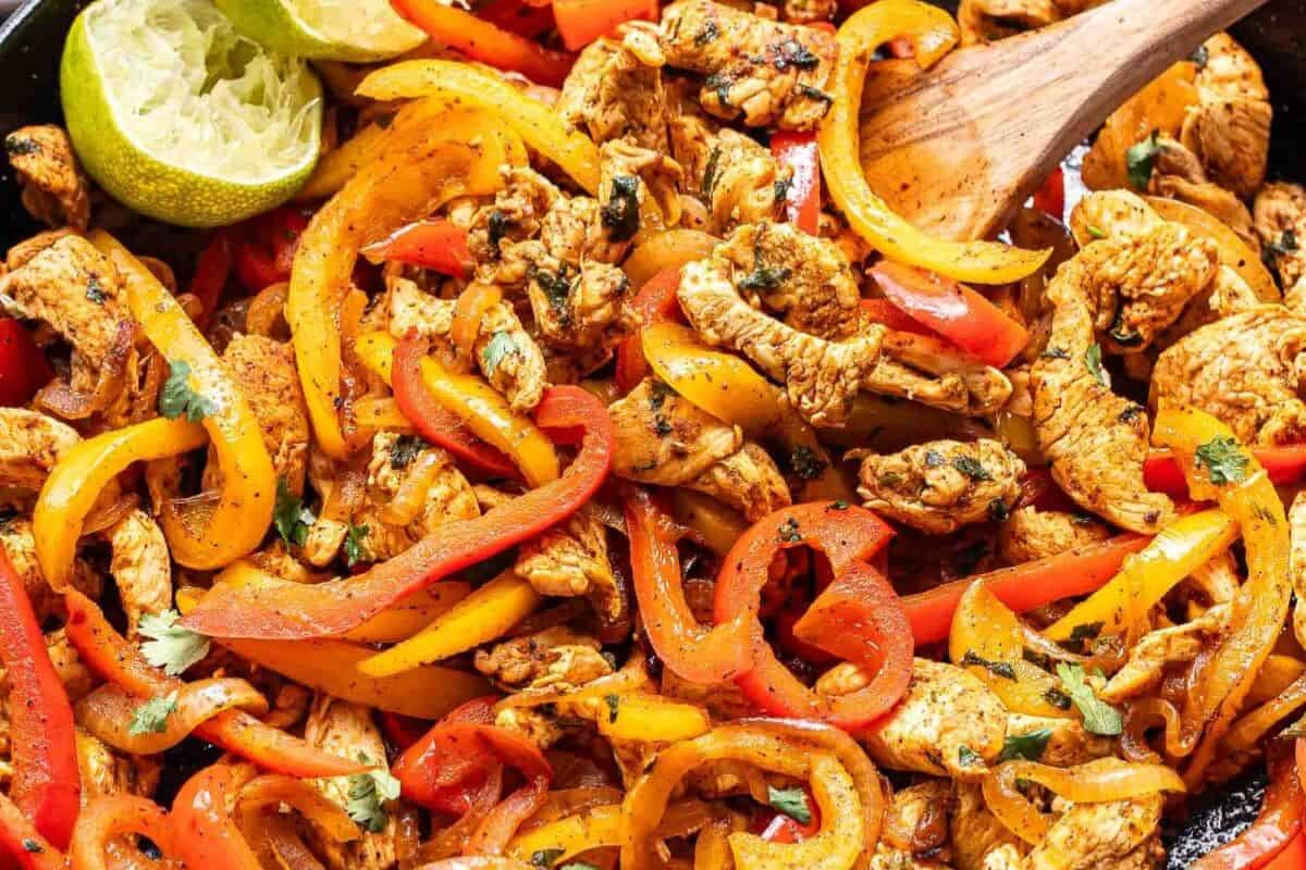 Chicken fajitas with strips of red and yellow bell peppers, garnished with cilantro, in a cast iron skillet with a halved lime—perfect for those seeking flavorful cast iron recipes.