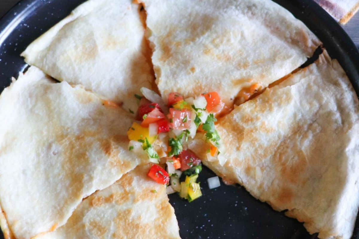 A cheese quesadilla cut into four pieces, garnished with a small serving of fresh salsa in the center, and served on a dark plate—a simple yet satisfying breakfast or dinner classic among cast iron recipes.