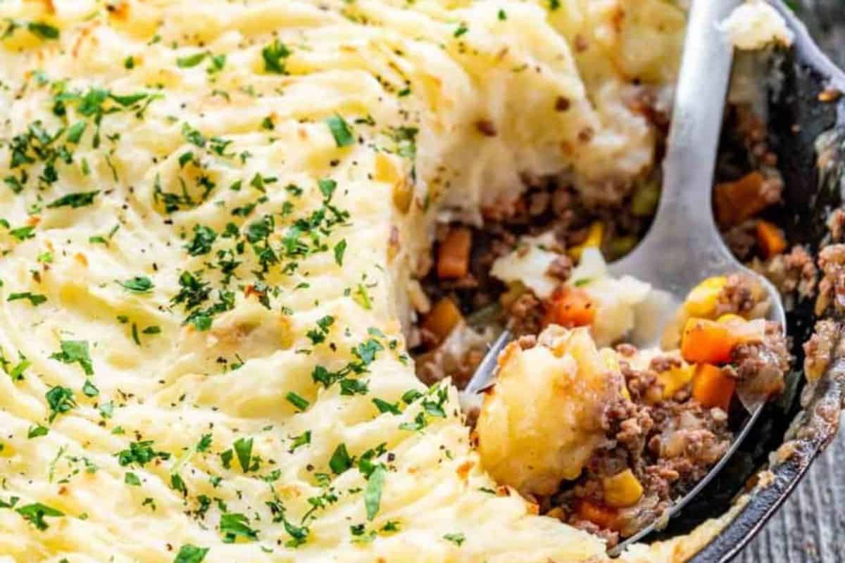 A serving of shepherd's pie being scooped out, revealing layers of mashed potatoes, ground meat, corn, peas, and carrots with parsley on top—a comforting classic among dinner recipes.