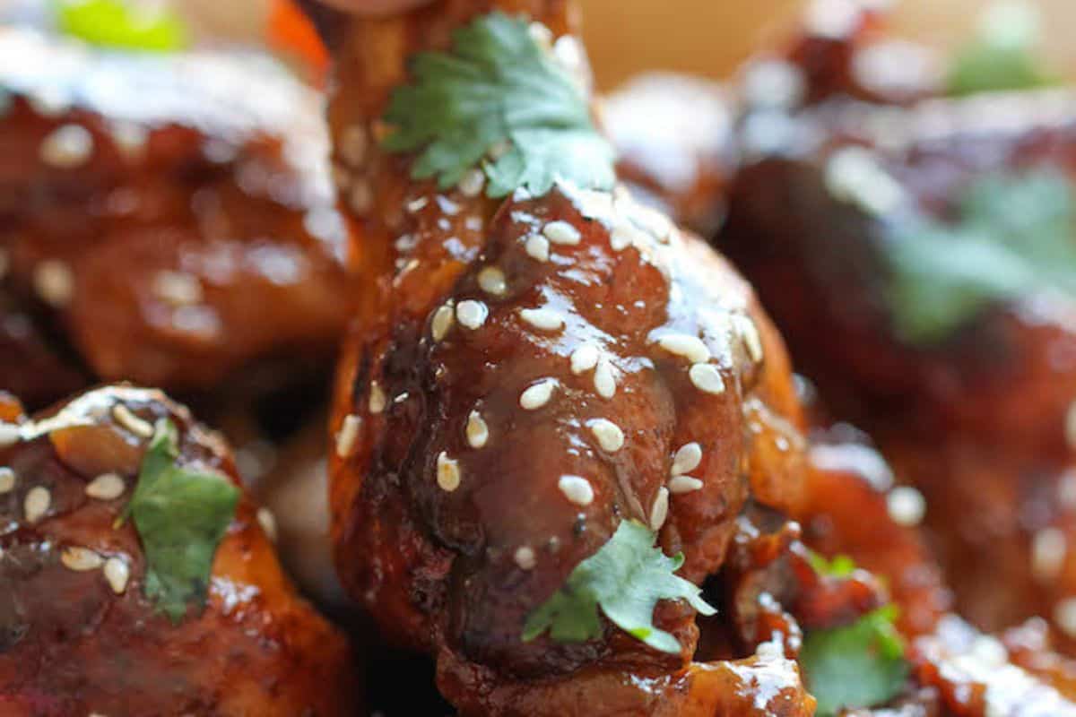 Close-up of glazed chicken wings sprinkled with sesame seeds and garnished with cilantro leaves—a game day favorite worth trying straight from your collection of delectable wing recipes.