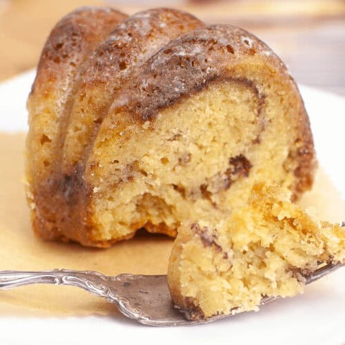 A slice of marble bundt coffee cake rests elegantly on a white plate, accompanied by a polished fork.