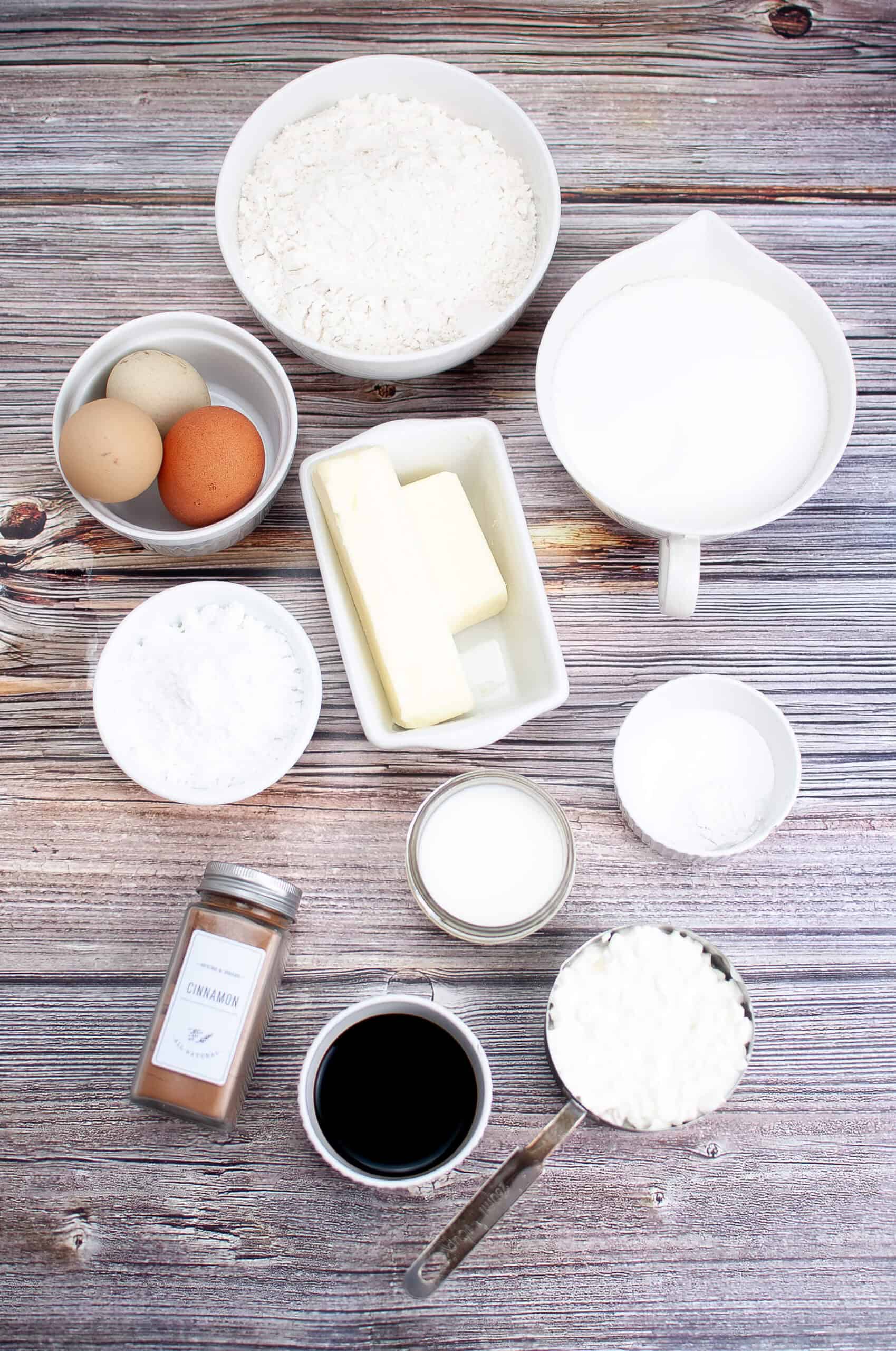 A wooden surface displays the classic ingredients for a Bundt coffee cake: flour, sugar, butter, eggs, vanilla, cinnamon, and milk.