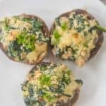 Three Stuffed Mushrooms filled with spinach, Boursin cheese, and herbs are artfully arranged on a white plate.