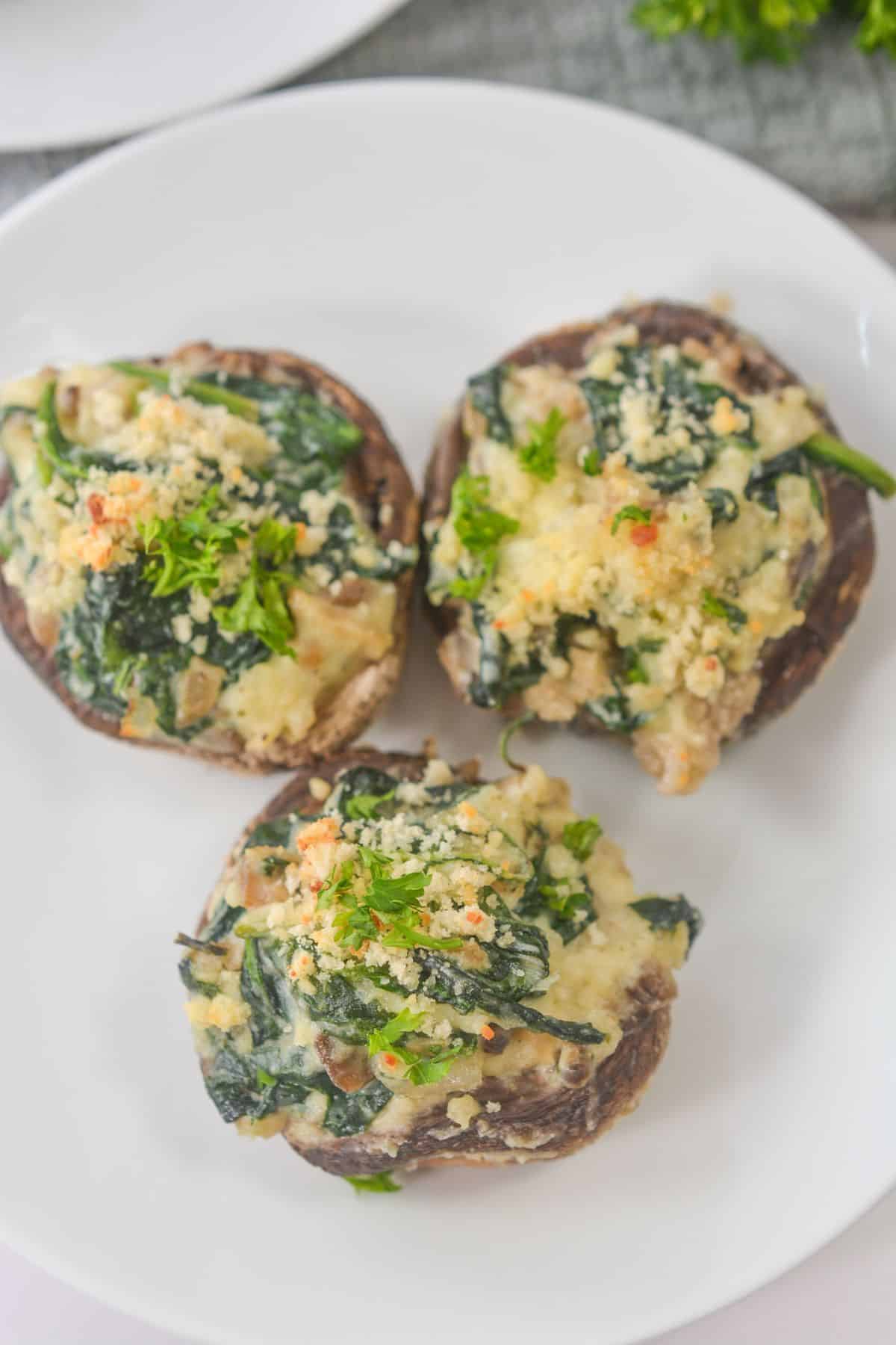 Three Stuffed Mushrooms filled with spinach, Boursin cheese, and herbs are artfully arranged on a white plate.