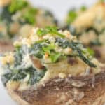 A close-up of a boursin cheese stuffed mushroom cap topped with spinach, breadcrumbs, and herbs sits elegantly on a white plate.