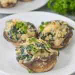 Three boursin cheese stuffed mushrooms filled with spinach and topped with breadcrumbs, served on a white plate. Parsley garnish in the background.