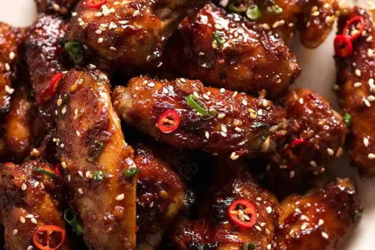 Close-up of glazed chicken wings garnished with sesame seeds, chopped green onions, and sliced red chili peppers.