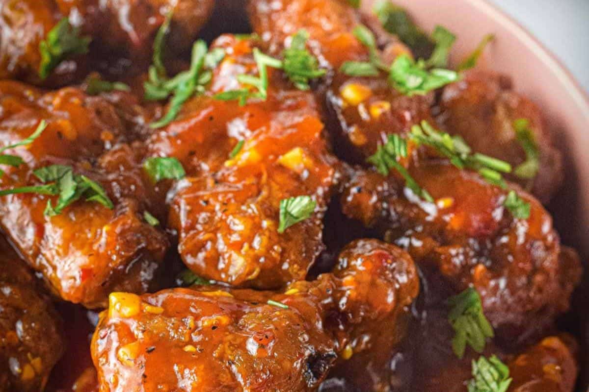 Close-up of saucy, glazed chicken wings garnished with chopped herbs in a dish.