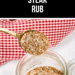 A spoonful of steak rub is held over an open jar, with the rich aroma mingling in the air against a backdrop of a red and white checkered cloth.