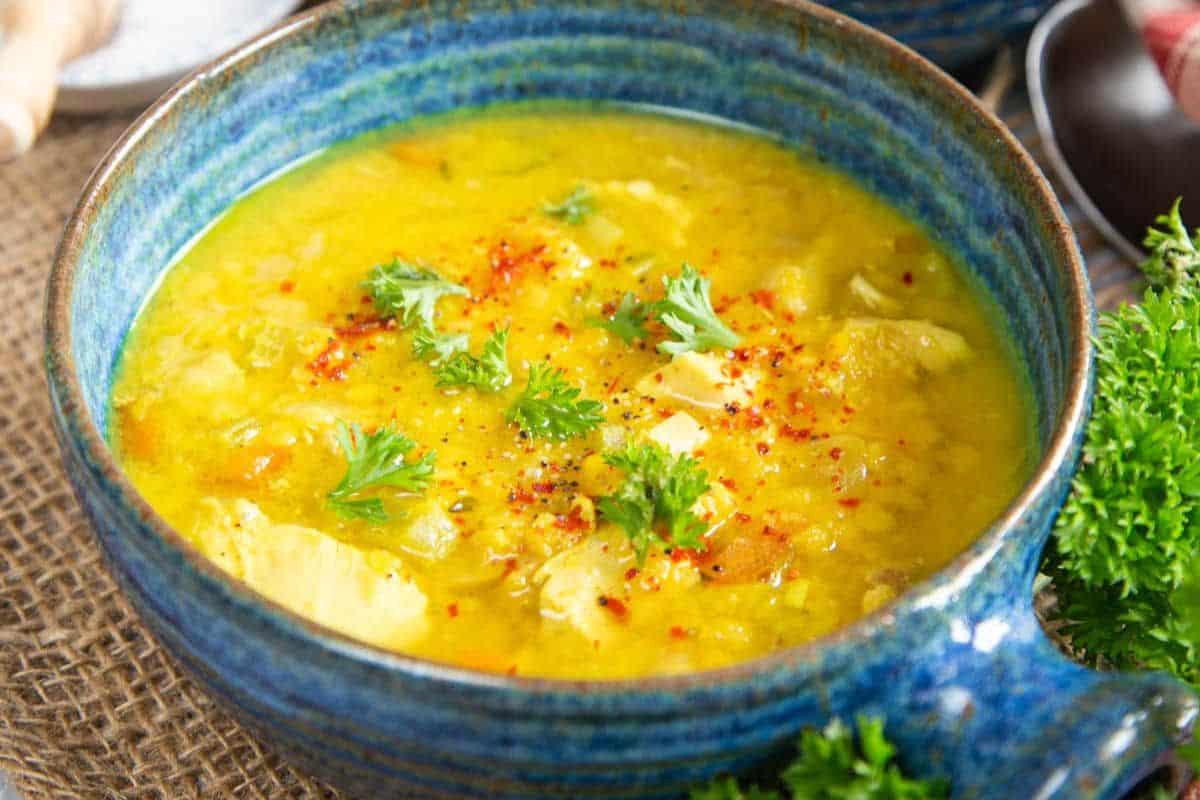 A close-up of a blue bowl of turkey and lentil soup, garnished with some parsley.