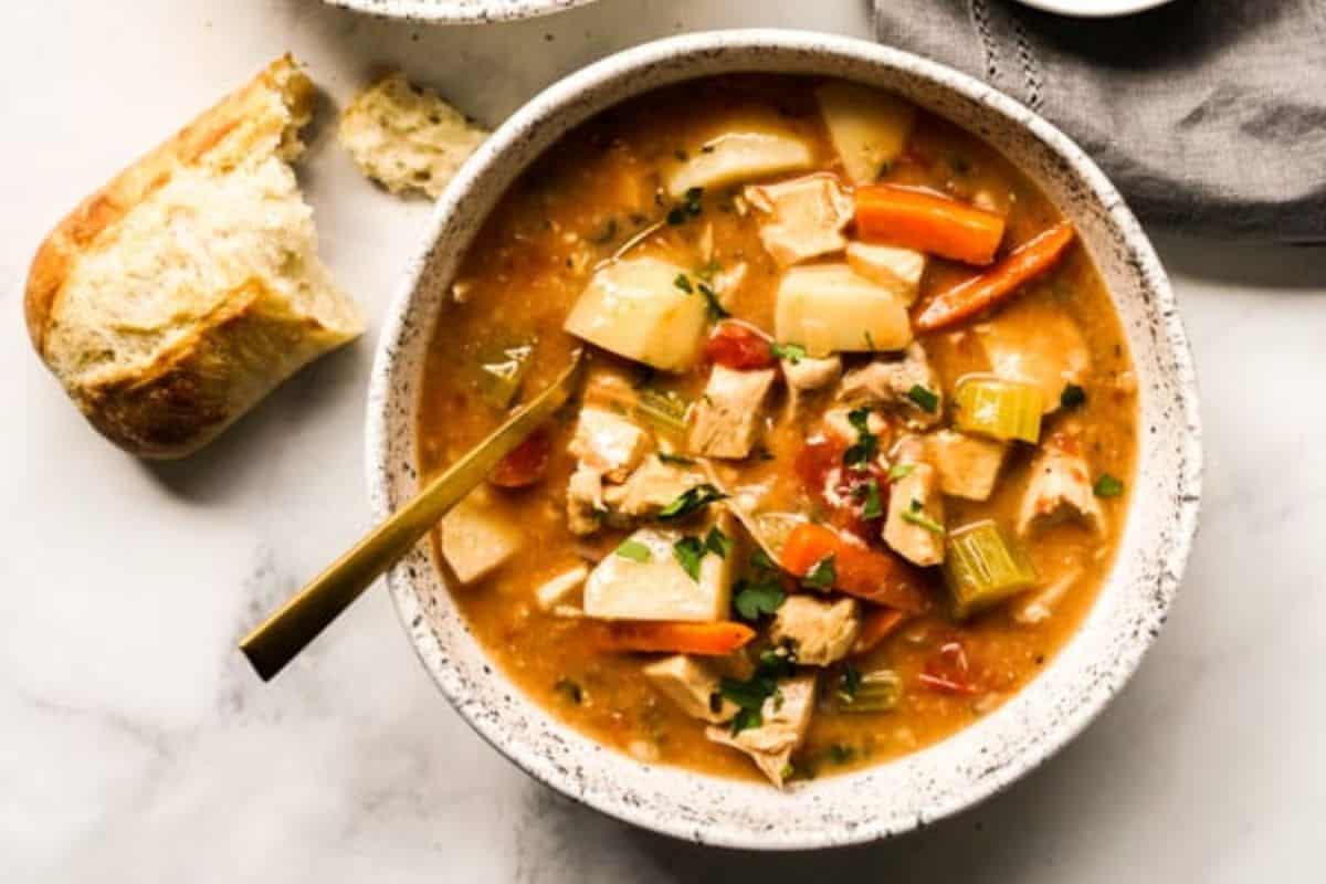 Close-up of a bowl of turkey stew, with peppers and celery and a piece of bread on the side.
