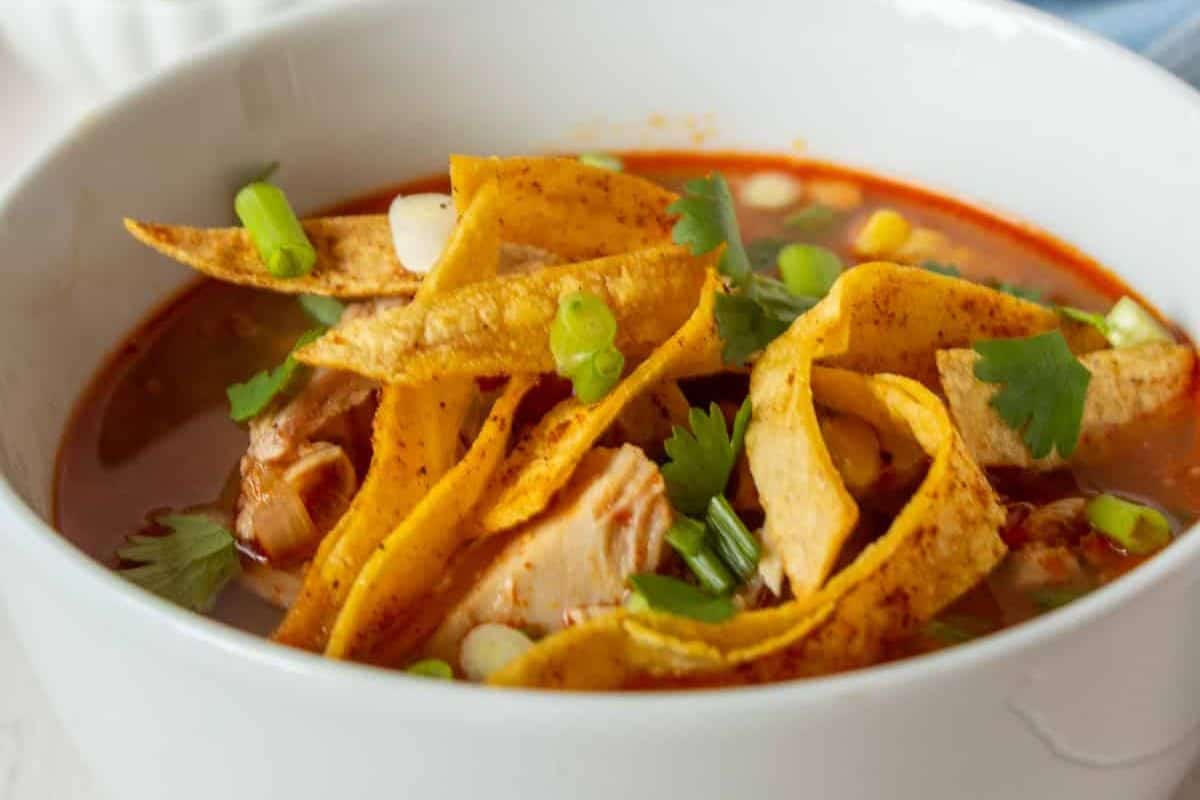 A close-up of a bowl of turkey tortilla soup, topped with yellow seasoned corn tortilla strips.