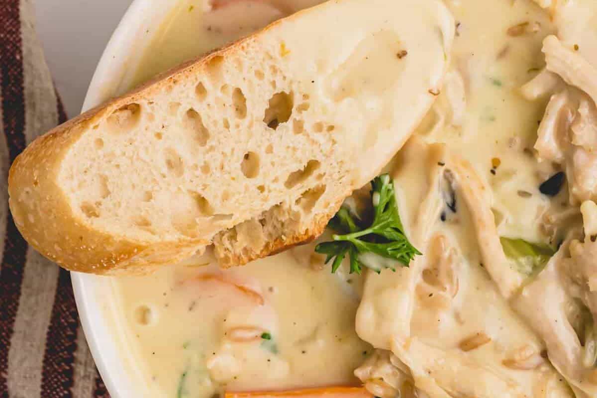 A close-up of creamy turkey and wild rice soup, with a crusty piece of bread for dipping on the side.