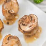 Close-up of mushroom-topped meatballs with rich gravy on a white plate, reminiscent of classic veal marsala flavors, garnished with fresh parsley.
