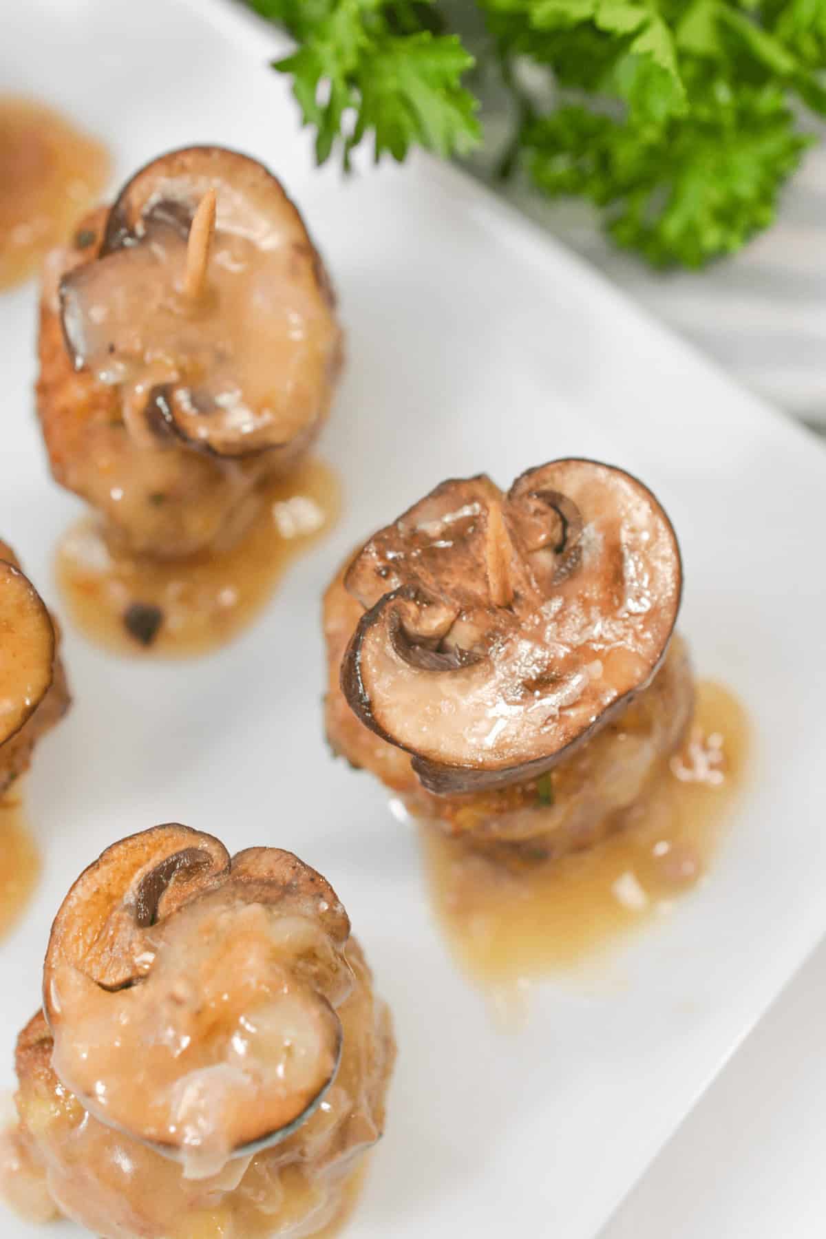Close-up of mushroom-topped meatballs with rich gravy on a white plate, reminiscent of classic veal marsala flavors, garnished with fresh parsley.