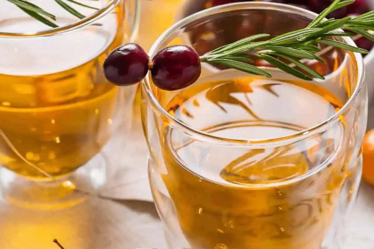 Glasses of apple boilo garnished with sprigs of rosemary.