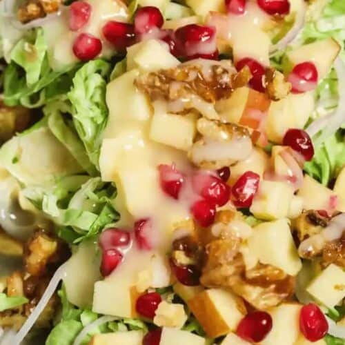 A close-up of a hearty winter salad with lettuce, walnuts, pomegranate seeds, apple chunks, and a creamy dressing captures the essence of the season.