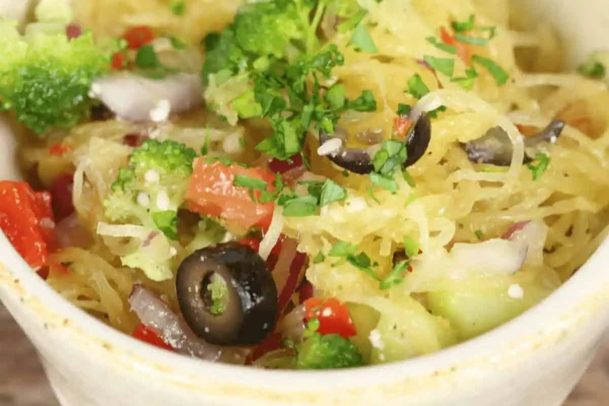 A bowl of spaghetti squash mixed with chopped broccoli, red bell pepper, red onion, black olives, and garnished with fresh parsley—perfect for those seeking flavorful squash recipes and delicious seasonal recipes.