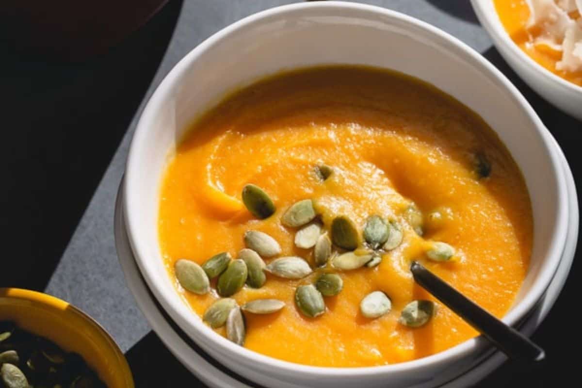 A bowl of orange squash soup topped with pumpkin seeds, with a spoon resting inside—perfect for those who love seasonal recipes.